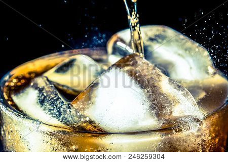 Stream Of Soda Being Pouring Into A Glass With Soda And Ice Cube On Black Background, Closeup Textur