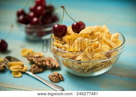 Tasty Cornflakes With Walnut And Cherry In Glass Bowl On Blue Background. Corn Flakes Healthy Breakf