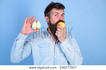 Man Bearded Eats Fruit, Holds Apple Blue Background. Half Of Apple Healthy Lifestyle. Hipster Demons