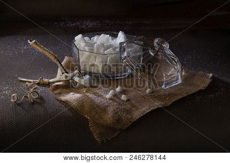 Old Nippers For Splitting Lump Sugar And Glass Sugar Bowl With Lid On Dark Background