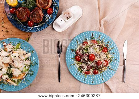 A Caesar Salad Fried Meat With Boiled Corn And Meat Rolls Are Served On The Table With The Beige Tab