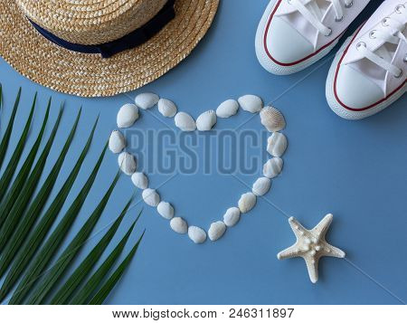 Shells, Sea Ster, Sneakers, Tropical Leaf And A Summer Hat On The Sea Blue Background. Minimal Summe