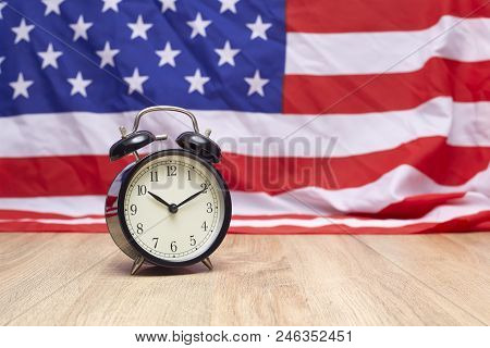 National flag of America and black alarm clock on old wooden background