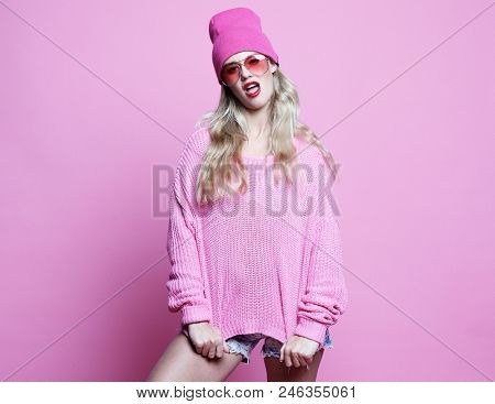 Stylish fashion portrait of trendy casual young woman in pink pulover and hat, posing over pink background.