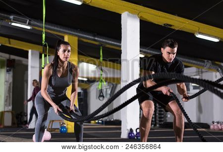 young fit sports couple working out in functional training gym doing  battle ropes cross fitness exercise