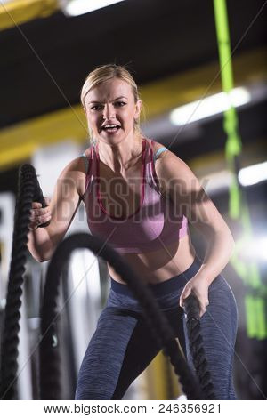 young fit athlete woman working out in functional training gym doing  battle ropes exercise as part of cross fitness training