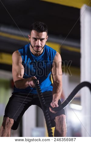 young fit athlete man working out in functional training gym doing  battle ropes exercise as part of cross fitness training