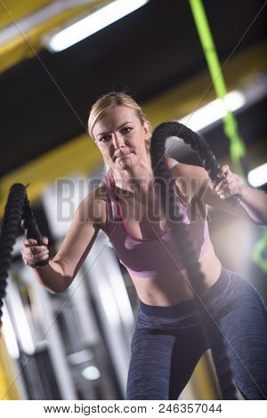 young fit athlete woman working out in functional training gym doing  battle ropes exercise as part of cross fitness training
