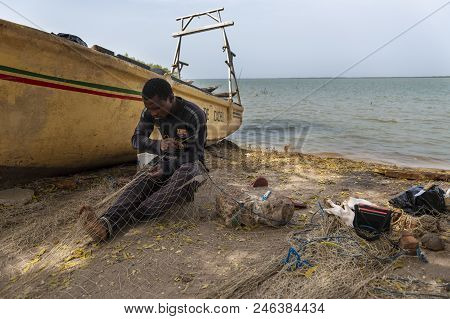Cacheu, Republic Of Guinea-bissau - February 1, 2018: Fisherman Repairing Fishing Nets In The Port O