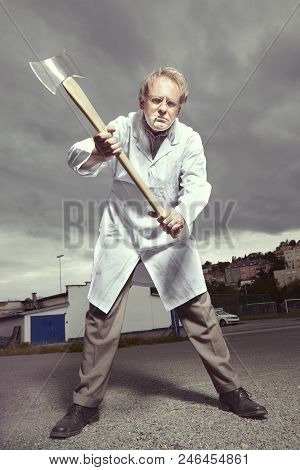Older Paramedic Freak Man In Medical Coat And Protective Helmet Threating With Double Axe