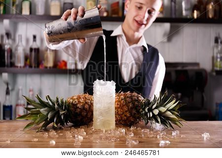 A Handsome Barman Is Pouring Alcohol Into A Pina Colada Coctail, Made Of Ripe Pineapples.