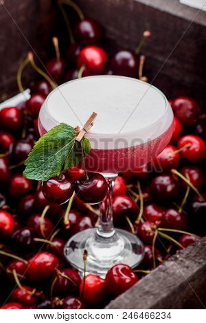 pink cocktail in Margarita glass with foam on top decorated with mint in cherry box. berry background