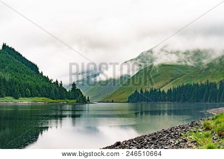 View Of A Beautlful Lake Talla In Scottish Borders With Green Hills Covered By Thick Rainy Clouds.