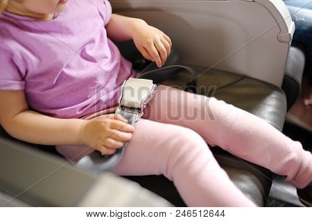 The Little Girl Sits In A Passenger Chair Of The Plane. Entertainments For Children On The Plane.