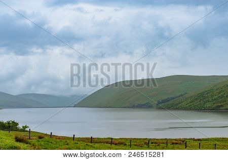 View Of A Beautlful Lake Talla In Scottish Borders With Green Hills Covered By Thick Rainy Clouds.