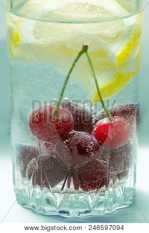 Cool Non-alcoholic Drink With Lemon Lobules And Cherries In Air Bubbles In A Glass On Blue Backgroun