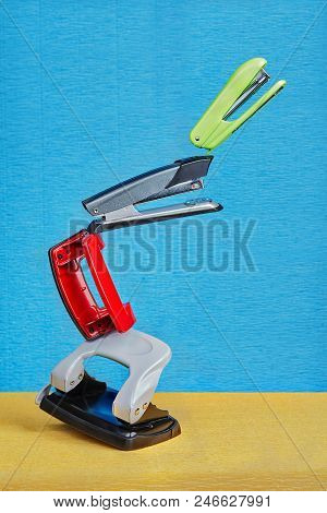 Few Colored Hole Punchers And Staplers Float In Air Under Non Gravity Conditions On A Blue Backdrop.