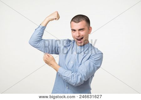 Handsome Middle Age Man In Blue Shirt Pointing Biceps Expressing Strength And Healthy Life. He Is St