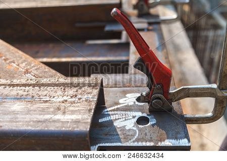 The Clamping Metal Clamp With A Red Handle Is Mounted On A Metal Plate