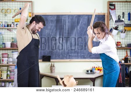 Two Caucasian Ceramists Squarrel And Crashing Clay Bowl On Table In Front With Rolling Pins. Negativ