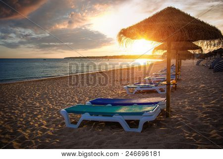 Row of beach straw umbrellas and deck chairs at sunset light