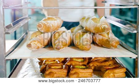 Baker Putting A Tray With Fresh Buguettes On Steel Rack At Commercial Kitchen Of Bakery, Close-up. B