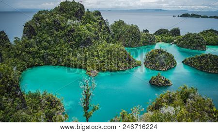 Blue Bay With Pianemo Island Overgrown With Jungle Plants, Surrounded By Shallow Blue Ocean Lagoon. 