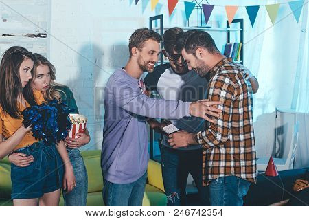 Smiling Young Man Holding Passport And Ticket While Standing With Friends At Farewell Party