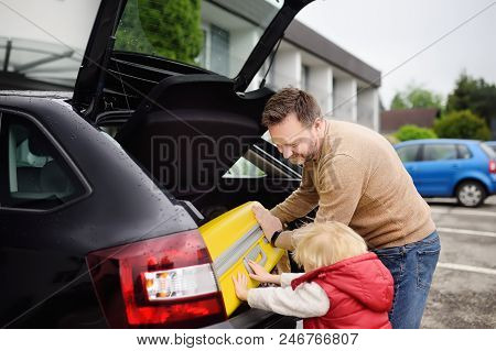 Handsome Man And His Little Son Going To Vacations, Loading Their Suitcase In Car Trunk. Automobile 