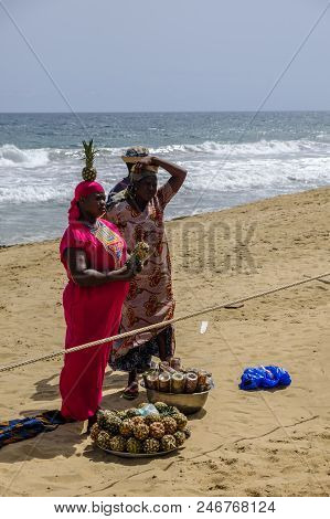 Grand Bassam, Cote Divoire - April 9 2018: Woman In Bright Pink Dress Balances A Pineapple On Her He