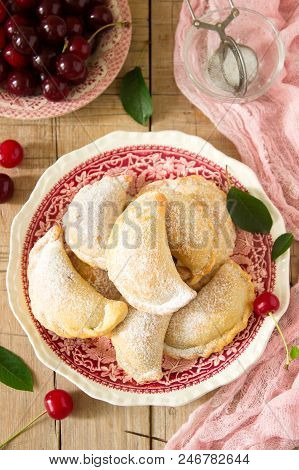 Pies With Cherries, Sprinkled With Powdered Sugar And Berries Of Fresh Cherries On A Wooden Surface.