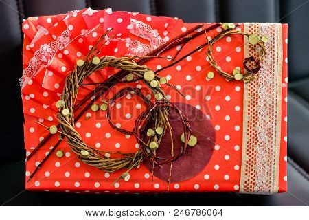 Handmade Gift Box Wrapped With Red Paper And Decorated With Dried Twigs On Dark Leather Sofa. Top Vi