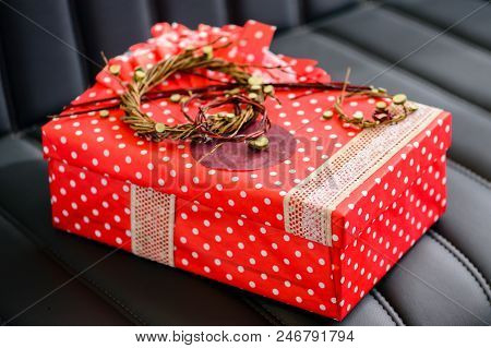Handmade Gift Box Wrapped With Red Paper And Decorated With Dried Twigs On Dark Leather Sofa