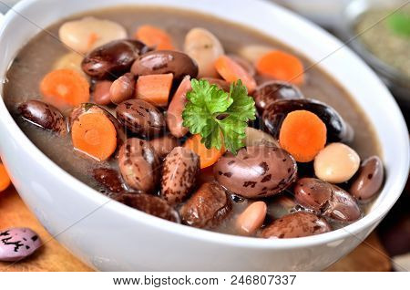 Close-up Of Bean Soup With Large Beans On Cutting Board, Carrots, Parsley, Marjoram, Spoon And Ladle