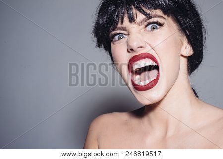 Enraged Female In Black Wig Screaming, Madness Concept. Young Woman With Furious Face Isolated On Gr
