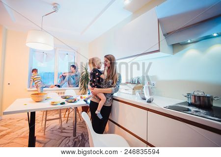 Parents And Kids Sitting Near Window And Having Fun At Kitchen. Smiling A Lot