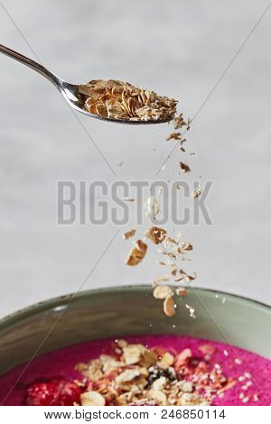 oat flakes in a spoon over a red smoothie in a pial on a concrete background