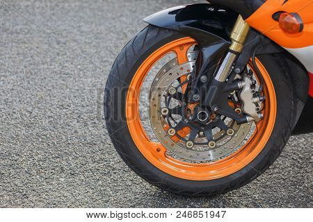 A Powerful Wheel Of The Orange Bike Is Standing On The Straight Grey Road.