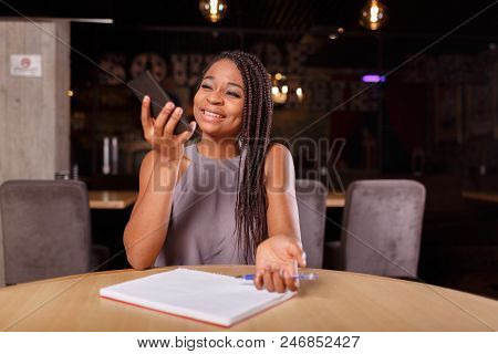 A Good-looking Afro-american Woman With Dreadlocks Is Looking At Her Phone Screen In The Cozy Cafe.