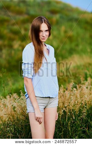 Happy Smiling Young Girl In Blue Shirt And Shorts In The Field