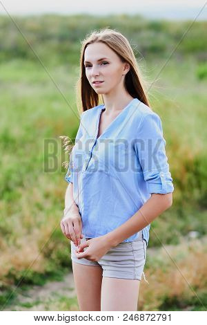 Happy Smiling Young Girl In Blue Shirt And Shorts In The Field
