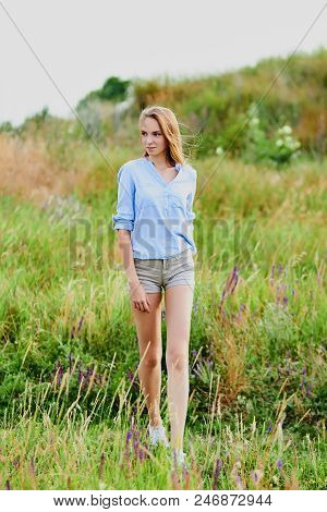 Happy Smiling Young Girl In Blue Shirt And Shorts In The Field