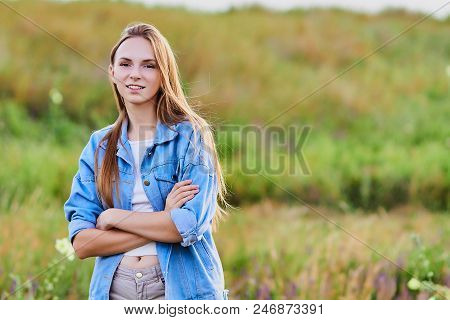 Happy Smiling Young Girl Wearing Blue Jeans Jacket And Shorts Is Standing In The Field