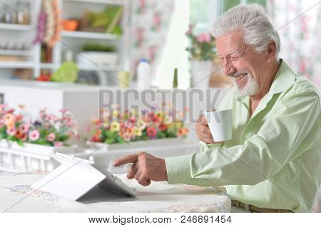 Emotional Senior Man Looking At Digital Tablet While Drinking Tea