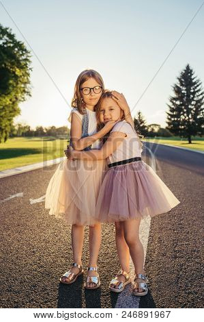Two Attractive Girls Standing On The Road And Hugging. Sisters And Friends Love Concept.