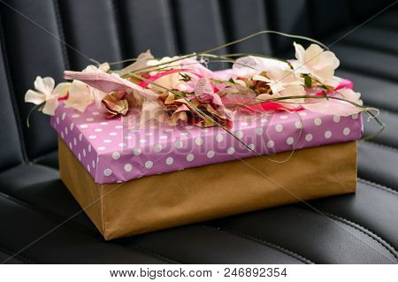 Handmade Gift Box Wrapped With Pink Paper And Decorated With Ribbon And Flowers On Dark Leather Sofa