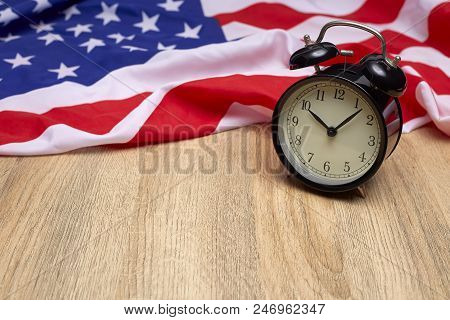 National Flag Of America And Black Alarm Clock On Old Wooden Background
