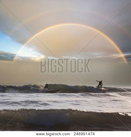 Silhouette of surfers on wave, stormy sky in the background