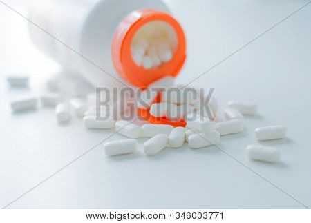 White Tablets Spilling Out Of A Plastic White Bottle With A Tablet