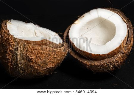 Two Halves Of Broken Coconut Lie On A Black Background